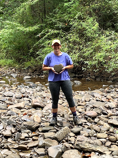 Patti in purple shirt on the river bed holding a heart-shaped rock